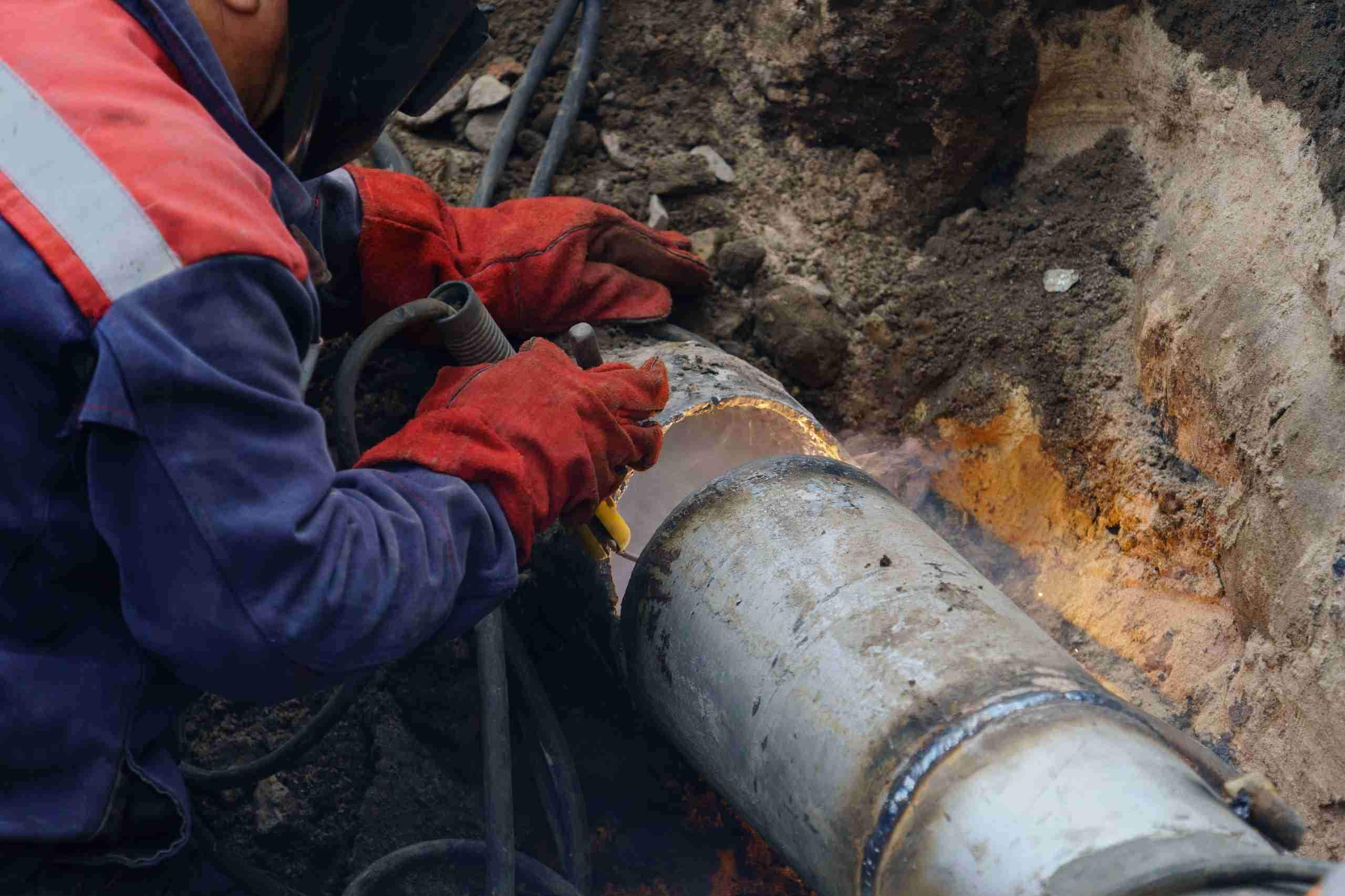 A worker welds a large metal pipe underground